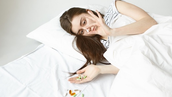 Avis médical sur la sécurité des somnifères pendant la grossesse : photo d'une femme allongée se couvant avec un drap blanc et tenant des cachets