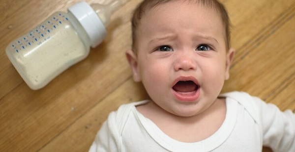 Bébé agité pendant le biberon :photo d'un bébé garçon allongé, portant un haut blanc à côté d'un biberon à moitié vide.