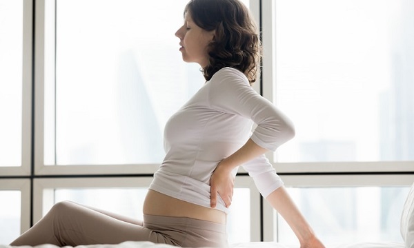 Changements dans le développement au cours du deuxième trimestre: photo d'une femme enceinte portant un vêtement à manches longues blanc, assise et tenant le dos.