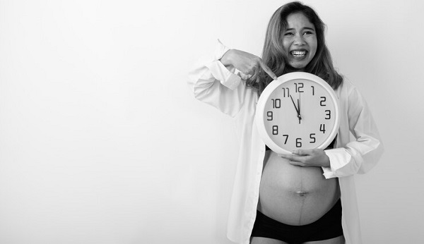 Compte à rebours pour la maternité: photo d'une femme enceinte en chemise blanche tenant une horloge.