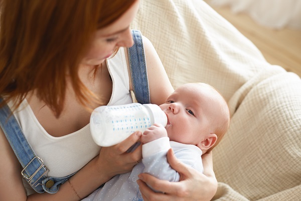 Conseils pour faire la transition entre l'allaitement maternel et l'alimentation au biberon ,bébé reposant dans les bras de sa mère, qui suce du lait maternel dans un biberon