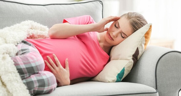 Effets secondaires du stress pendant la grossesse: photo d'une femme enceinte en tee-shirt rouge allongée sur un canapé.