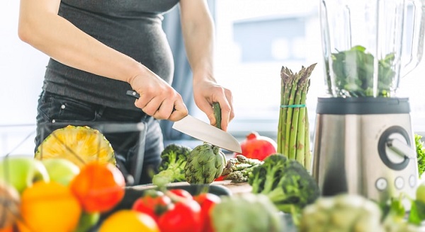 Mangez l'alphabet: photo d'une femme enceinte devant plusieurs aliments sains et tenant un couteau.