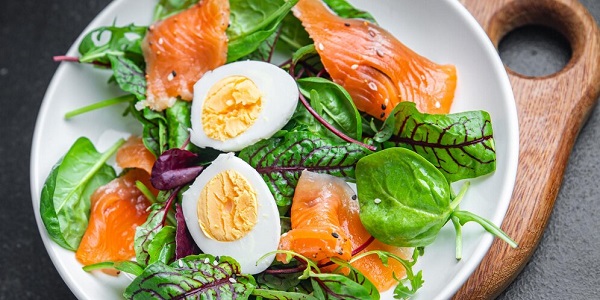 Mise en service: photo des feuilles vertes, saumons et oeufs durs sur un plat blanc.