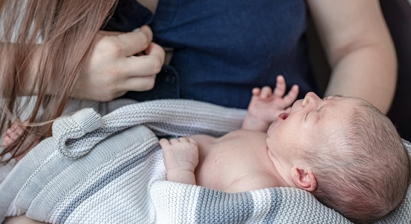 Pourquoi mon bébé pleure-t-il après la tétée: photo d'un nouveau né en train de pleurer, placé dans une couverture et tenu par la mère.