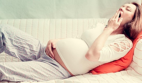 Pourquoi le sommeil prénatal est-il si épuisant: photo d'une femme enceinte qui baille en train de s'allonger sur un canapé.