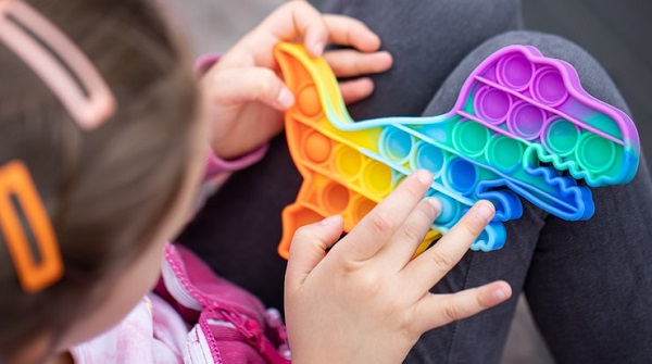 Concentre sur l'acceptation de l'autisme de ma fille, mais pas sur la guérison: photo d'une petite fille tenant un jouet dinosaure anti stress multicolore