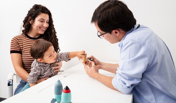 À quel âge l'autisme peut-il être détecté: photo d'un petit garçon assis sur sa maman évalué par un medecin