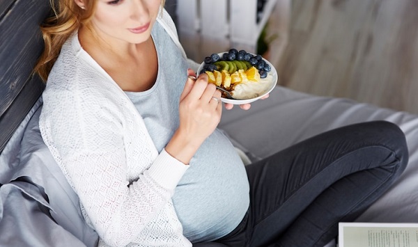 Des alternatives saines pour satisfaire les envies de la grossesse: photo d'une femme enceinte assise en tenant un plat rempli de salade de fruits