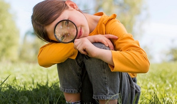 Pourquoi les enfants autistes se perdent dans les détails: photo d'une petite fille en tunique jaune moutarde tenant une loupe