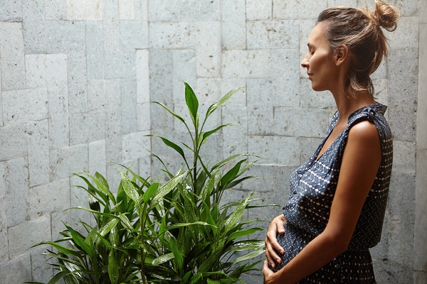 une femme enceinte tendre et joyeuse qui se détend devant une plante verte