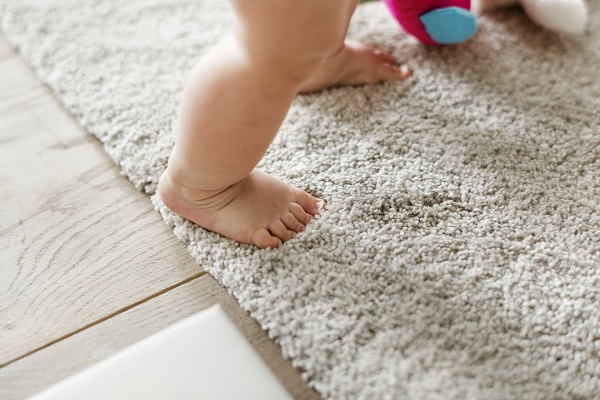 quand bébé marche, pieds de bébé debout sur un tapis avec un bout de sa peluche