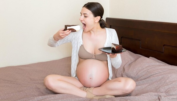 La science derrière vos envies de manger pendant la grossesse: photo d'une femme enceinte assise et tenant 2 morceaux de gateau