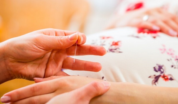 La vérité holistique sur l'acupuncture et la grossesse: photo d'une main tenant une aiguille en train de piquer une autre main.